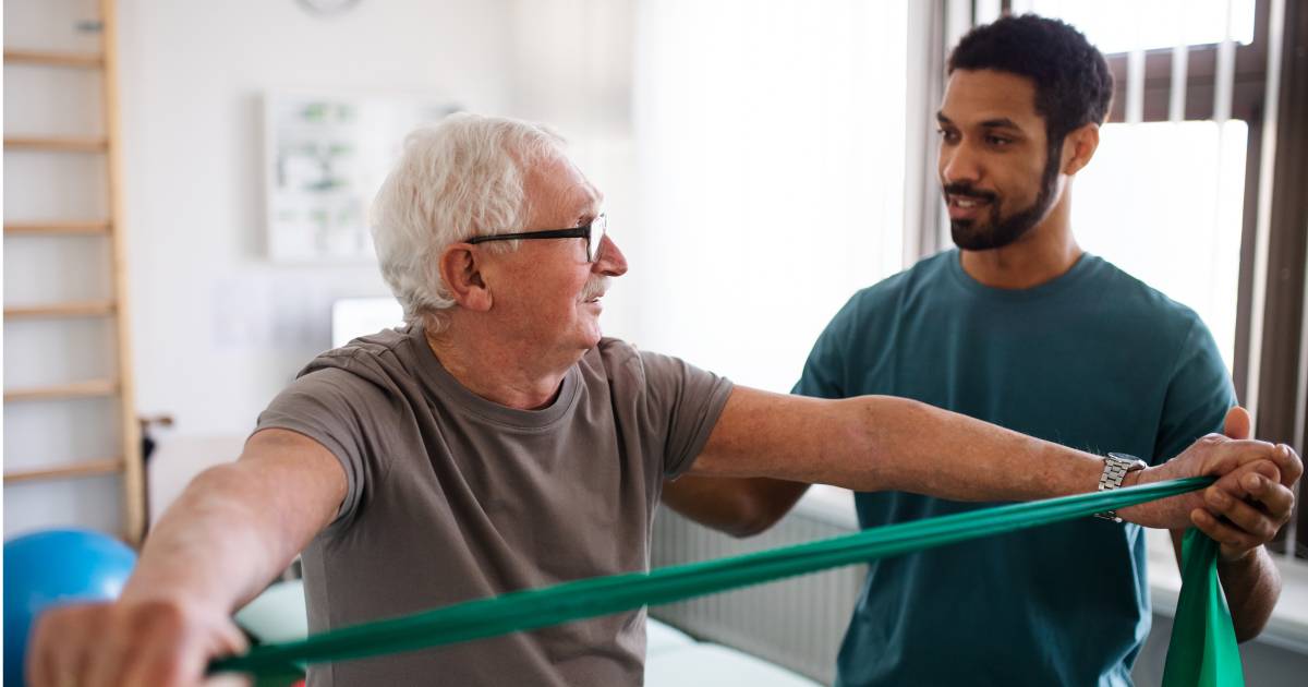 physical therapist with elderly man using green stretchband
