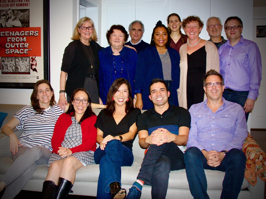 group of people sitting on a couch cmiling at the camera. There is a second row behin them with more poeple smiling.