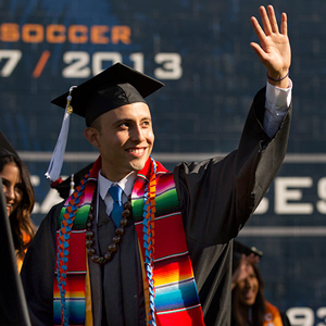 Hispanic graduate waving at commencement.