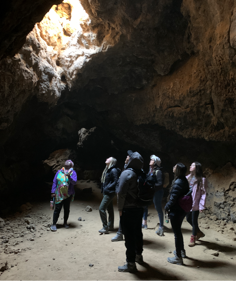 Studies students explore a lava tunnel looking upwards towards the light